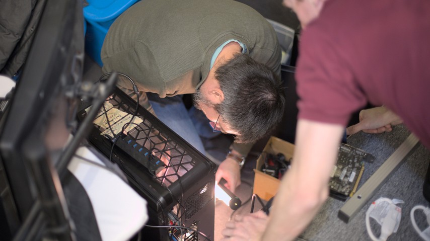 A photo of Rubén Rodríguez Pérez and Ian Kelling swapping out video cards during LibrePlanet 2023.